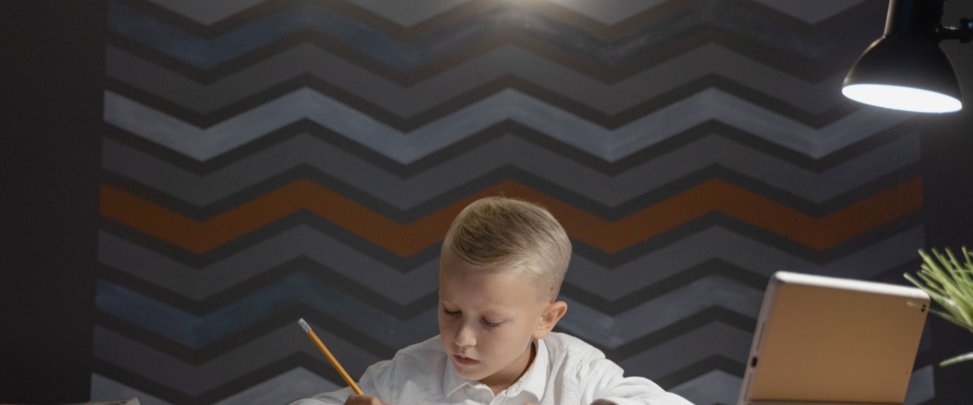 Dreng laver lektier ved et skrivebord med lampe