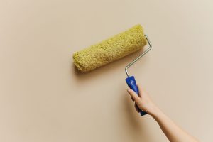 Hånd med malerrulle, der maler en beige væg